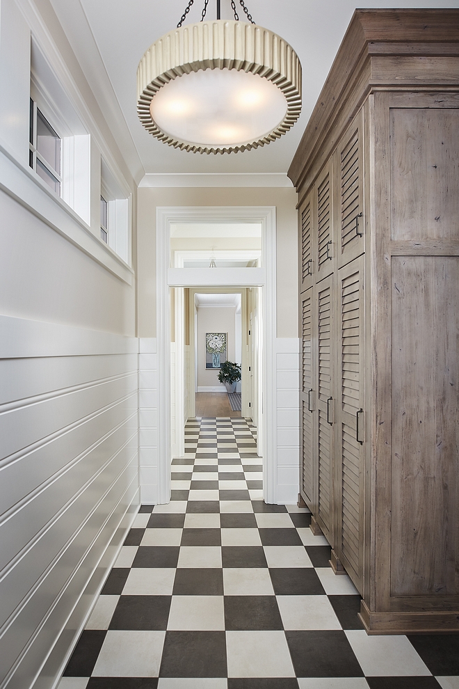 Mudroom featuring a large custom mudroom cabinet with louvered doors, an Arteriors pendant light and classic black and white checkered floor in a matte finish #mudroom #mudroomcabinet #mudroomfloor #mudrooms