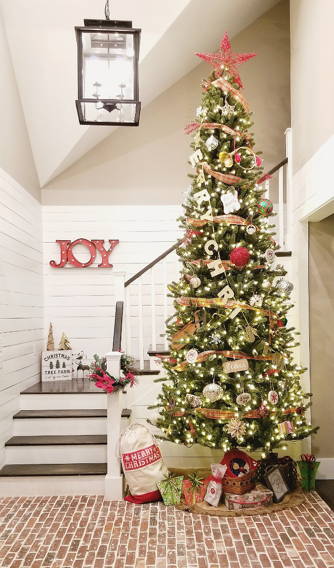 Farmhouse Christmas Tree 12 foot Christmas tree now stands tall in the foyer with brick flooring and shiplap walls The styling is classic farmhouse with little pops of patterns and assortment of reds #FarmhouseChristmasTree #Farmhouse #ChristmasTree #brickflooring #shiplap #brick