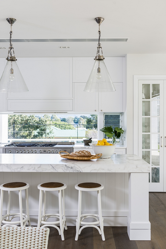 White kitchen with thick countertop and chunky island posts Glass windows behind the range gives an airy feel to this entire kitchen #kitchen #thickcountertop #chunkyislandposts
