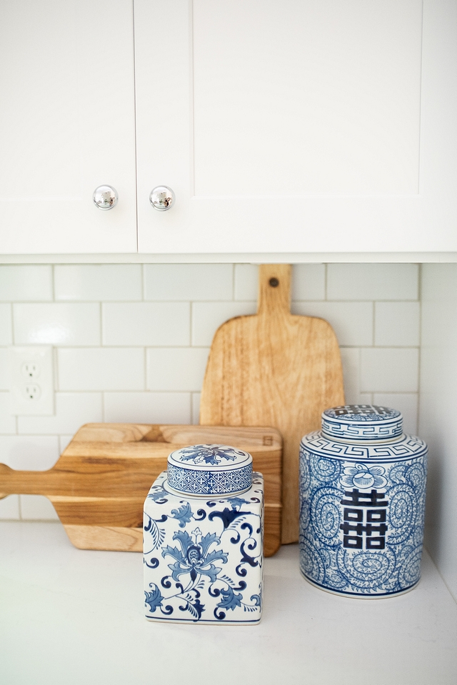 Kitchen Decor Kitchen countertop decor with blue and white ginger jars and wooden cutting boards on white quartz countertop and white subway backsplash White Cabinet paint color is SW Pure White