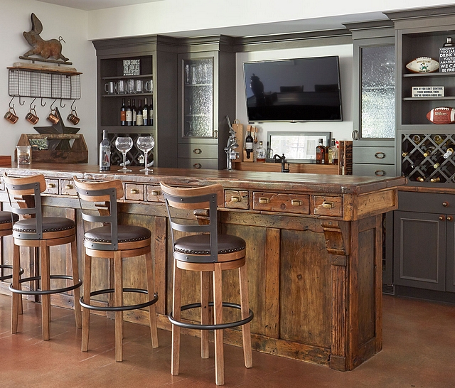 Rustic Wood Antique Bar with Gray Perimeter Cabinets The antique bar was locally sourced. The perimeter cabinets are alder with a flint finish and features seeded glass door inserts and built in wine storage #bar #cabinet #barcabinet #bardesign #barideas #winestorage #rusticinteriors #distressedcabinet #rusticcabinet
