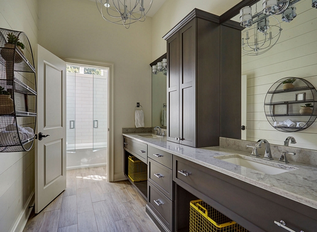Bathroom features a neutral color scheme with warm white shiplap walls, dark wood vanity with his and her sinks and wood-looking porcelain floor tile #Bathroom #neutralcolor #colorscheme #shiplap #darkwoodvanity #woodlookingporcelaintile