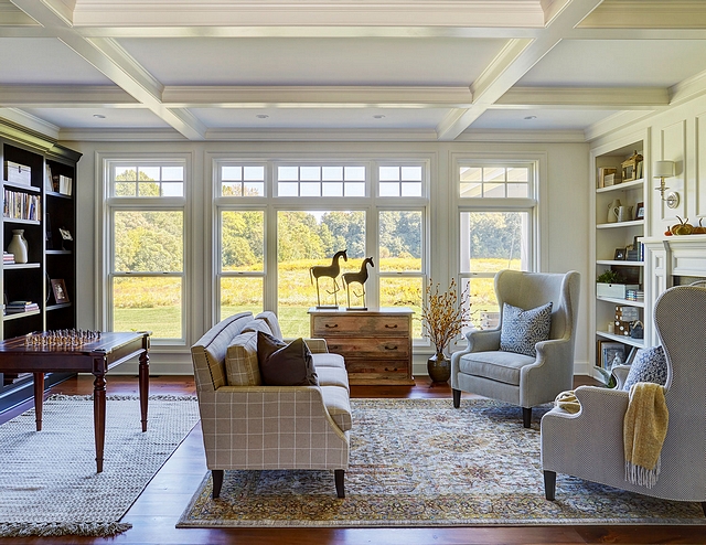 The kitchen opens to a cozy living room with coffered ceiling, wide plank pine flooring, and upholstered wingback chairs Wall color is Sherwin Williams Eider White #livingroom #cofferedceiling #SherwinWilliamsEiderWhite #livingroom