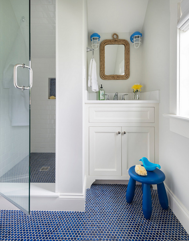 Cottage Kids Bathroom. This cottage kid's bathroom features a white washstand under a Two's Company Know Your Ropes wall mirror and white and blue cage sconces. The walk-in shower has sloped ceiling tiled with white subway tiled and a blue hex tiled shower floor. #Kids #bathroom #Cottage Digs Design Company.