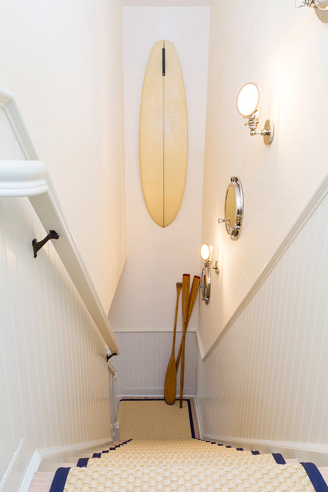 Staircase. Hallway gallery to the home's second floor. Displayed is a vintage surfboard, nautical sconces and mirrors, and a collection of vintage oars. Custom sisal runner with navy blue binding adorn the bleached oak stairs. #Staircase #Coastal Chango & Co. 