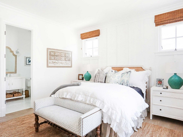 White coastal bedroom. White coastal bedroom with settee at the feet of the bed, linen bed, white nightstands, jute rug, hardwood floors, batten and board accent wall and bamboo shades. #CoastalBedroom #WhiteCoastalBedroom #CoastalInteriors 