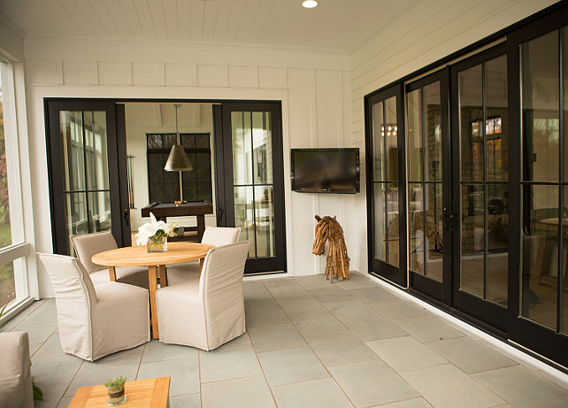 Sliding Doors to Screened in Porch. Black Glass sliding doors open to a screened in porch filled with a round teak dining table lined with slipcovered slipper dining chairs facing a corner flatscreen TV. Hahn Builders.