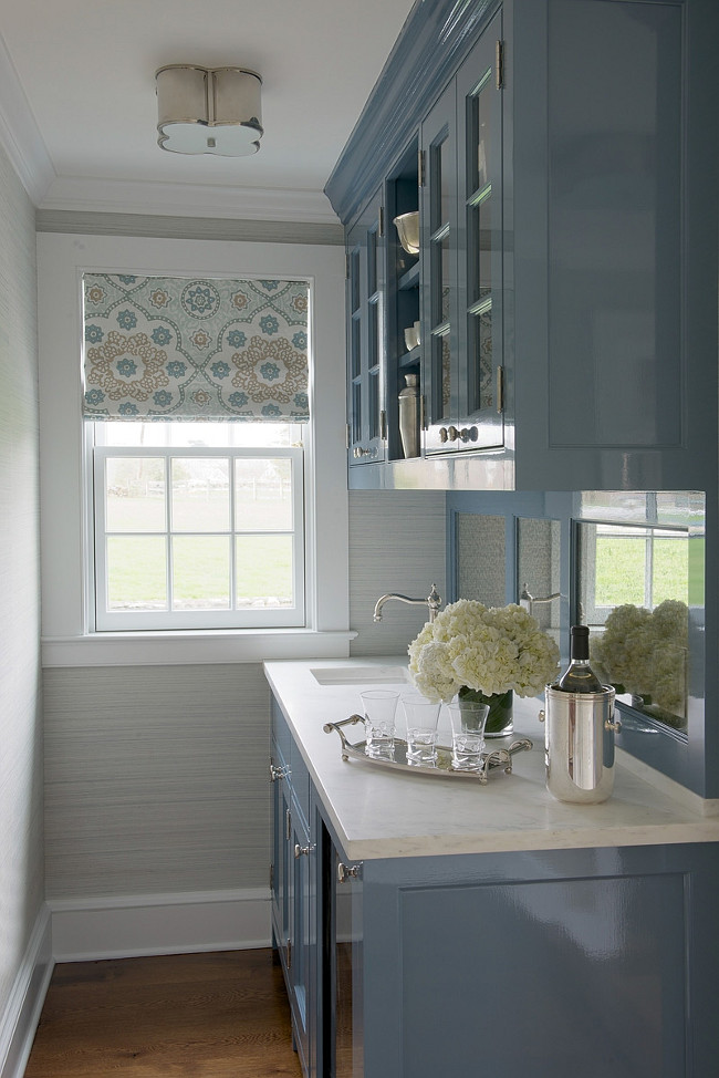 Blue butler's pantry design with Visual Comfort Lighting Basil Flushmount Light as well as high gloss blue cabinets paired with white marble countertops and mirrored backsplash. Chic butler's pantry features glass-front upper cabinets and blue cabinets accented with mini wine cooler and small prep sink with vintage style faucet. #Blue #Butlerspantry Kerry Hanson Design.