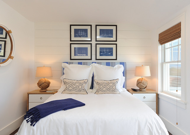 Blue and White bedroom. Coastal Blue and White bedroom. Beach house Blue and White bedroom. Nautical Blue and White bedroom. Nautical bedroom with shiplap clad accent wall featuring framed sailboat blueprints over a blue striped headboard on bed layered with white bed linens topped with blue sailor knot pillows and a blue fringed rug throw. A pair of two-tone nightstands stand on either side of the bed topped with Pottery Barn Rope Knot Table Lamps with a Serena and Lily Montara Mirror.
