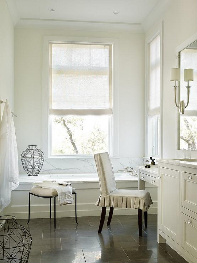 Bathroom. Transitional bathroom features an ivory wainscoted tub with a marble deck and backsplash placed under windows dressed in a natural linen roller shades. Interior Design by Beth Webb Interiors.