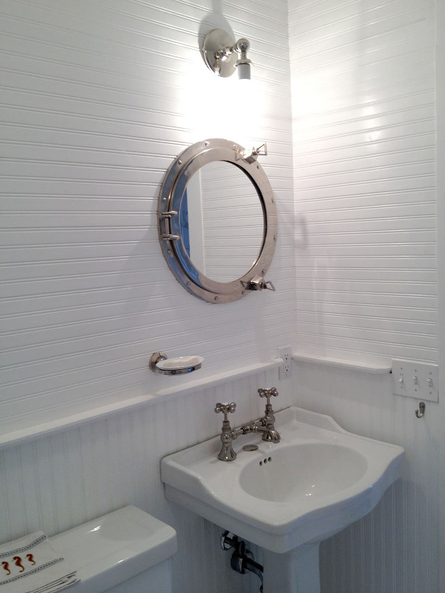 Beadboard Bathroom. White Beadboard Bathroom. Coastal Bathroom with White Beadboard Walls. The powder room features custom white beadboard walls and a coastal mirror. This porthole was sourced from a shipyard graveyard, refinished and converted into a medicine cabinet. Fits perfectly with the theme of the house. #Beadboard #Bathroom #WhiteBeadboard #BeadboardWall