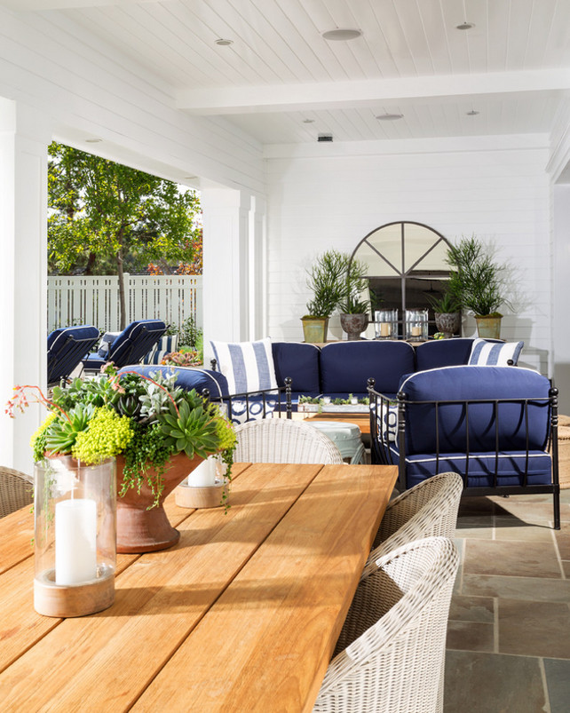 Covered patio. Covered patio layout. This loggia features beadboard ceiling and tongue and groove wall paneling framing a palladian mirror over rustic console table placed behind an outdoor blue sofa accented with denim blue striped pillows facing a reclaimed wood coffee table flanked by jute stools atop gray slate tiled floor. Legacy Custom Homes, Inc.