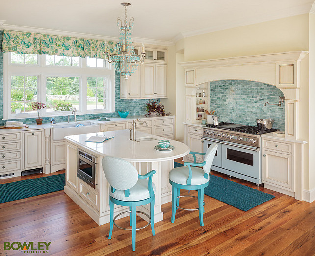 Kitchen. Coastal Kitchen with creamy white cabinets, turquoise backsplash, turquoise chandelier, turquoise counterstools and turquoise roman shades. #Kitchen #CreamyWhiteKitchen #TurquoiseKitchen #Turquoise Bowley Builders