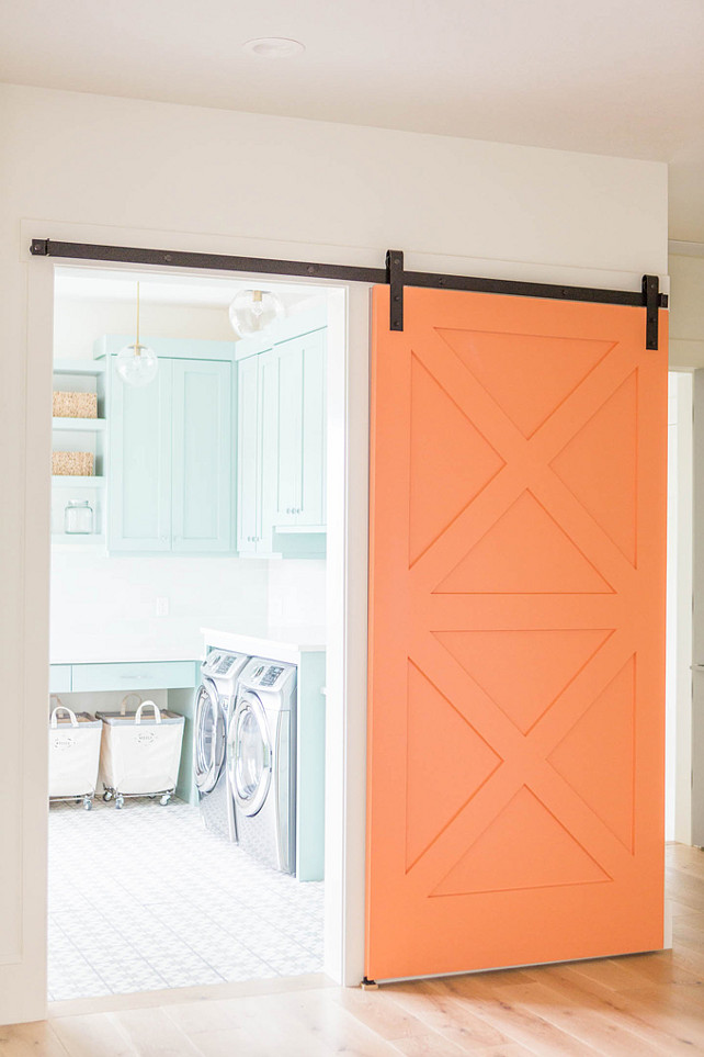Laundry room with barn door. Laundry room with barn door ideas. An orange barn door on rails slides open to reveal a laundry room. #LaundryRoom #BarnDoor Ashley Winn Design.