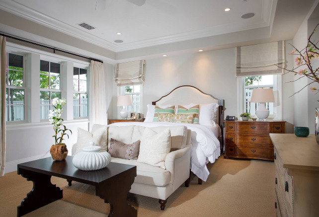 Master bedroom. Master bedroom design. Great idea of adding a natural linen settee. Notice the damask pillows and espresso coffee table. This beautiful master bedroom features arched bed dressed in soft white bedding and gray and mint green striped pillows flanked by traditional nightstands placed under windows. The windows are dressed in gray grosgrain roman shades. #MasterBedroom Legacy Custom Homes, Inc.