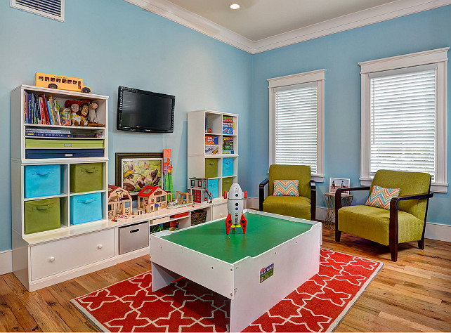 Playroom. chevron pillows, green armchairs, open shelves, Play Table, recessed lighting, red and white area rug, storage bins, toy storage, wall mounted TV, white blinds, white shelving unit, white trim