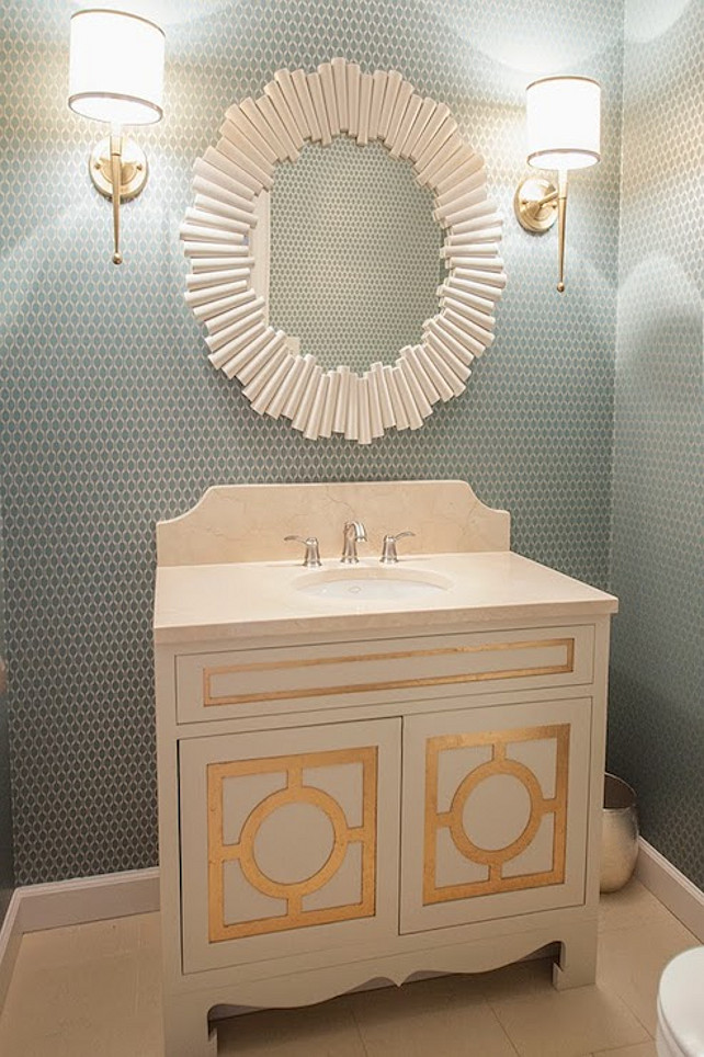 Powder Room. Powder Room Design. Transitional Powder Room. Chic powder room features walls clad in blue and ivory geometric wallpaper which frame a Charles Round White Mirror flanked by contemporary sconces over a custom vanity accented with gold leaf molding light stone counter and a matching backsplash. #PowderRoom Lucy and Company
