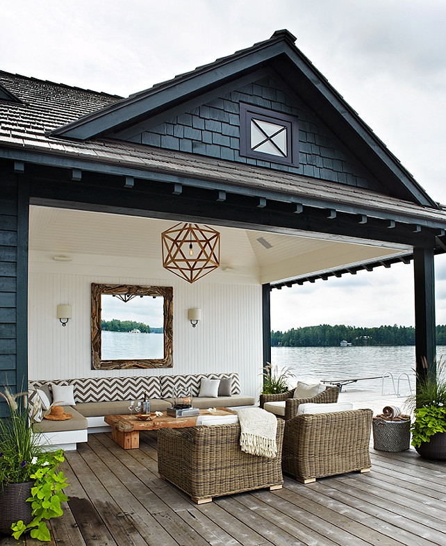 Lakeside Covered Patio. Lakeside cottage covered deck with beadboard ceiling and wood polyhedron pendant. White beadboard walls with rectangular driftwood mirror flanked by iron ring sconces with half moon shades. Outdoor sectional sofa upholstered in white and tan chevron cushions. Driftwood coffee table, wicker outdoor chairs and plank deck floors. Anne Hepfer Designs.