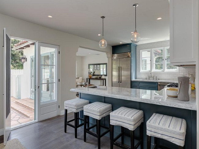 Peninsula kitchen kitchen features blue cabinets paired with white and grey quartzite countertops and a white subway tiled backsplash accented with dark grout. A pair of glass pendants hang over a blue kitchen peninsula lined with white and slipcovered backless counter stools. A kitchen sink and deck mount faucet stands next to an enclosed refrigerator. #Blueandwhite #Kitchen #Peninsula #Twotonedkitchen Sotheby's Homes