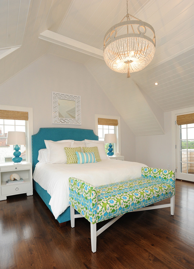 Bedroom. Beach House Bedroom Design. Beach House bedroom with a white Greek Key mirror reflecting a Ro Sham Beaux Frankie Beaded Chandelier hung over a peacock blue, nailhead trimmed headboard on bed layered in white bed linens topped with a pair of chartreuse pillows and an aqua blue striped pillow flanked by a pair of modern white nightstands topped with Robert Abbey Triple Gourd Lamps in Peacock. Nina Liddle Design.