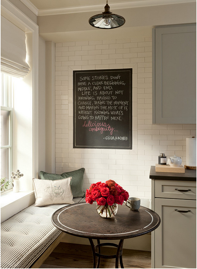 Breakfast Nook. Small Breakfast Nook. This small breakfast nook breakfast nook filled with a rustic bench doubling as window seat topped with a ticking stripe tufted cushion facing a round iron bistro table illuminated by vintage barn pendants alongside a kitchen chalkboard framed by subway tiles. #BreakfastNook Jenny Wolf Interiors.