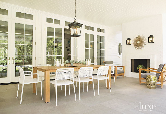 Patio with fireplace. White Kartell side chairs surround the Janus et Cie Mistra dining table on the loggia, while classic lantern fixtures add a formal touch. The pendant is by Charles Edwards, and the Vaughan Designs sconces above the fireplace are from Jasper Showroom. #Patio #fireplace Karen Putman.