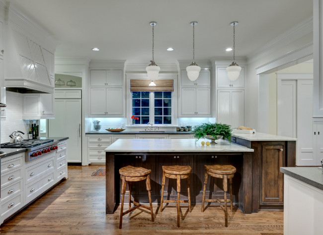 White kitchen with distressed island. The kitchen was designed with functionality in mind and includes pendants that were original to the home and respect past generations. New white cabinetry by Steve’s Cabinet Shop and countertops fabricated by Il Granito balance Theodore Alexander’s wood barstools from Brendan Bass Showroom. Linda Fritschy.