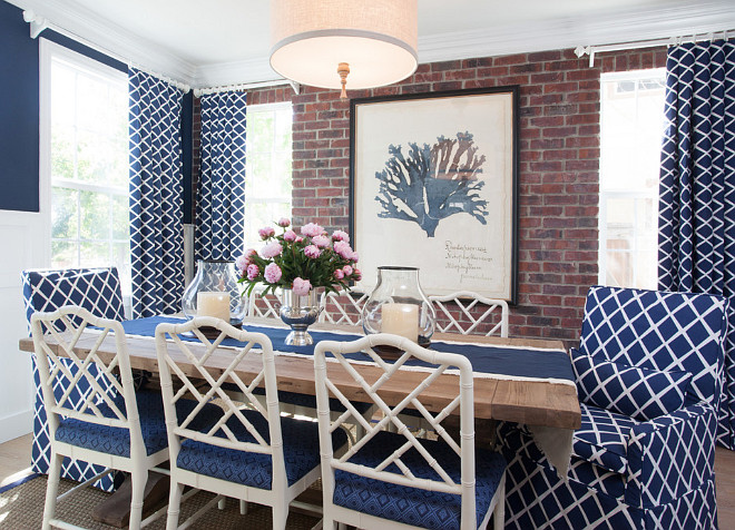 Coastal Blue and White Dining Room. Blue dining room features a linen drum pendant hanging over a salvaged wood dining table lined with white bamboo dining chairs accented with blue cushions against a backdrop of an exposed brick wall lined with a Natural Curiosities Capistrano Seaweed 1 flanked by windows dressed in blue lattice curtains. AGK Design Studio.
