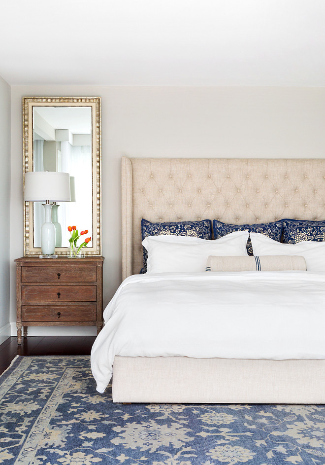 Bedroom. Master Bedroom. Blue and white decor in master bedroom. This stunning cream and blue bedroom features a linen tufted wingback bed dressed in white bedding and blue pillows next to a French nightstand. The headboard is from Restoration Hardware. The rug is from ABC Carpet in NYC. The master bedroom bedding is from Pottery Barn. Nightstand is from Arteriors Home. Mirror above night stand is from Ballard Designs #MasterBedroom #Bedroom #Decor Chango & Co. 