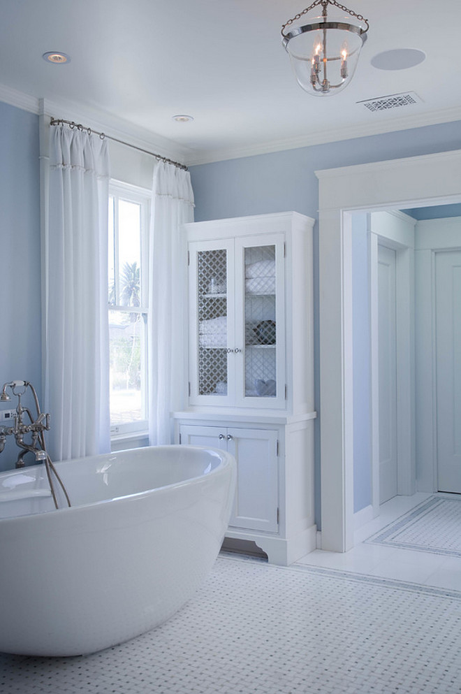 Bathroom Chicken wire cabinet doors. Blue and white bathroom with chicken wire cabinet. Blue spa like bathroom features walls painted blue lined with a chicken wire linen cabinet facing an egg shaped tub and vintage style tub filler atop basket weave tiled floor. #Blueandwhite #Bathroom #Chickenwirecabinet #Cabinet #Cabinetdoors Kim Grant Design Inc.