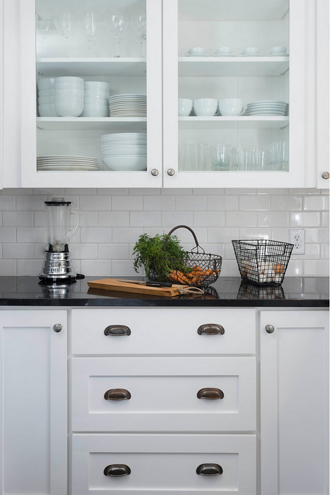 Farmhouse kitchen cabinet ideas. Simple farmhouse kitchen with white cabinet, black granite countertop, white subway tile backsplash and glass door upper cabinets. #Farmhousekitchen Tim Cuppett Architects. 