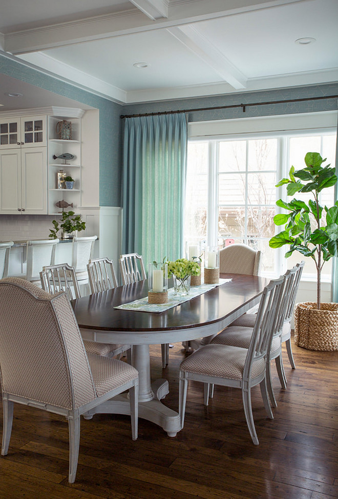 A large open concept kitchen and family room with full views from end to end The white kitchen, and its breakfast bar, open to a breakfast room surrounded by windows and moring light. The transitional regency style dining table and chairs have a distressed driftwood finish to keep the breakfast area sophisitcated but casual To the right is the continuation of the open concept family room 