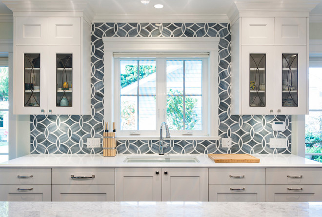 Eclipse glass cabinets. White and blue kitchen boasts white shaker cabinets painted Benjamin Moore White Heron paired with Princess White Quartzite countertops and an Ann Sacks Beau Monde Glass Polly Tiles in Absolute White and Pearl. A kitchen sink, Kohler Frost Blue Sink, with a Brizo Talo Faucet stands under windows flanked by eclipse glass cabinets #eclipseglasscabinets