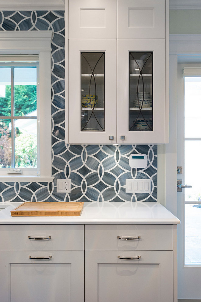 Blue tile backsplash. White and blue kitchen boasts white shaker cabinets painted Benjamin Moore White Heron paired with Princess White Quartzite countertops and an Ann Sacks Beau Monde Glass Polly Tiles in Absolute White and Pearl. A kitchen sink, Kohler Frost Blue Sink, is paired with a Brizo Talo Faucet flanked by glass eclipse cabinets. #Bluetilebacksplash #Bluebacksplash #Bluetile Sarah Gallop Design Inc.