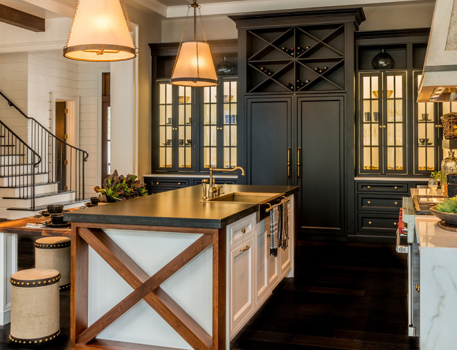 The designer painted the interiors of the black cabinets with the glass doors in white to create balance with the white island. The x based island is made of reclaimed wood and brings warmth to the kitchen island, while a dark stone countertop creates a cohesive look with the rest of the kitchen. #Xbaseisland #KitchenIsland Palmetto Cabinet Studio