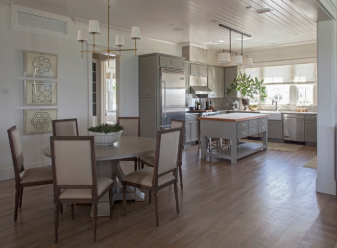 Open Dining room features a beadboard ceiling accented with an antique brass Bryant Chandelier illuminating a round gray dining table lined with French square back dining chairs; Restoration Hardware Vintage French Square Fabric Side Chairs. Artwork is Jean Baptiste Geometrics Art. The kitchen boasts gray cabinets paired with gray granite countertops and backsplash. A 3 drum pendant, Bryant Small Billiard Light, hangs over a gray kitchen island topped with butcher block lined with Tolix Stools. . #DiningRoomOpensto Kitchen #Kitchen #DiningRoom #OpenDiningRoom Urban Grace Interiors