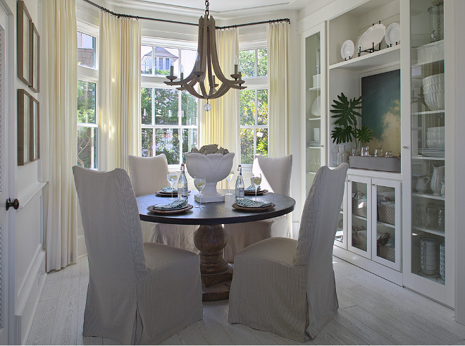 Bay window draperies. Dining room bay window drapery ideas. Beautiful cottage breakfast nook features bay windows dressed in cream curtains filled with round pedestal dining table lined with linen slipper dining chairs illuminated by an Arteriors Manning Chandelier atop white oak floors. Dining room bay windows with floor to ceiling draperies. #Baywindow #Baywindowdraperies #DiningRoomBaywindow #diningroom #Baywindowdarperyideas Urban Grace Interiors