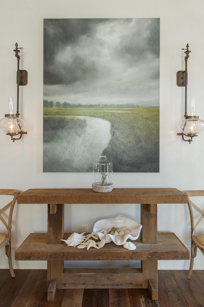 Rustic Coastal Foyer. Rustic Coastal Foyer Design and Decor. Walls are Venetian plaster painted in Benjamin Moore White Dove. Light Fixtures: custom by Eloise Pickard- old gas fixtures. Chairs: Constance side chairs from Ballard Designs. Console table is made of reclaimed wood. Artwork: "Storm over the Marsh". #RusticFoyer #RusticCoastal #Foyer #CoastalInteriors Interiors by Courtney Dickey and T.S. Adams Studio.