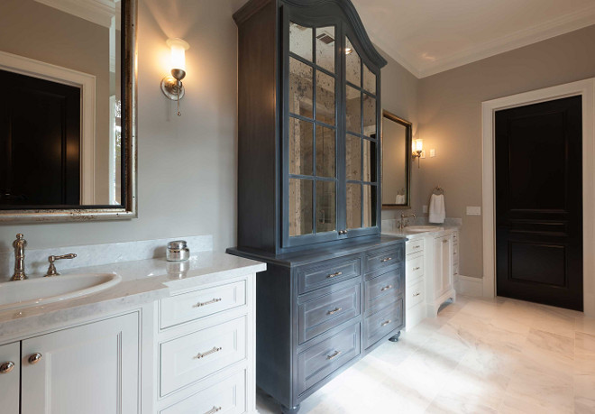 Bathroom. Bathroom boasts a dark gray distressed linen cabinet finished with antiqued mirrored doors flanked by his and her washstands. Master bathroom boasts separate washstands topped with white marble fitted with oval sinks and vintage style faucets placed under silver leaf beveled mirrors. Elizabeth Garrett Interiors