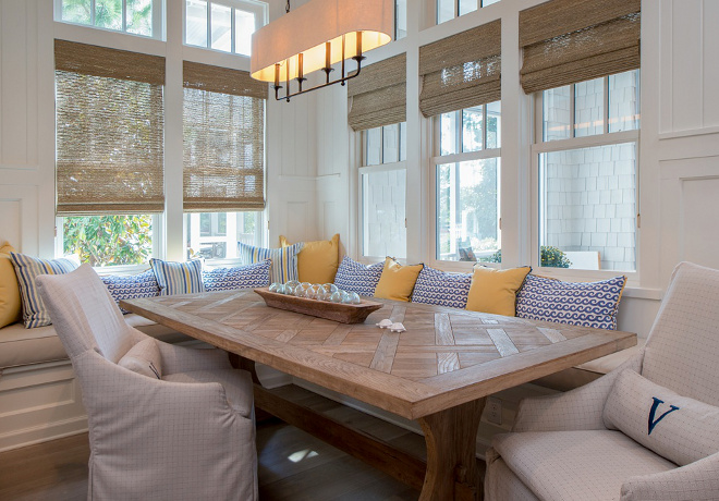 Dining Room Banquette. Forget big and formal dining rooms. Families want to feel close and united in a cozy - and gorgeous - banquette like this one! The custom pillows are in Kravet fabric, table is from Englishman’s Antiques, and the upholstered chairs are from Lee Industries; upholstered in Perennials indoor/outdoor fabric. The woven shades are custom. #banquette #casualdining #casualinteriors #interiros #coastalinteriors #wovenshades Interiors by Courtney Dickey of TS Adams Studio.