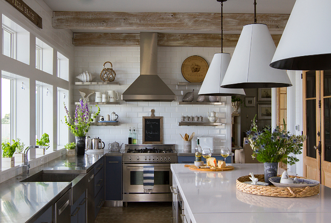 Rustic beach house kitchen with stainless steel perimeter countertop and white quartz kitchen island countertop. Whitewashed ceiling beams and floating shelves flank a stainless steel hood against white subway tile backsplash. Island countertop is White Zeus Quartz. #kitchen #rustickitchen #rusticinteriors #modernrustic #kitchenideas #kitchens 