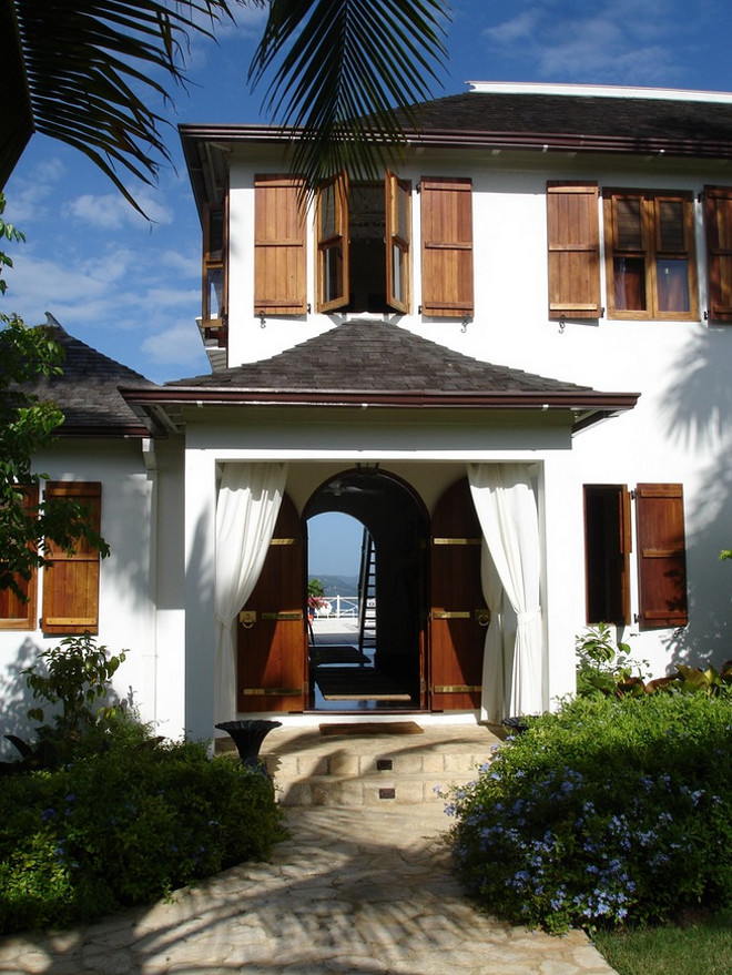 Home exterior arched door batten shutters casement windows front yard landscaping hip roof outdoor curtains portico shingle roof stone path stone steps white curtains white exterior Siegel Architects