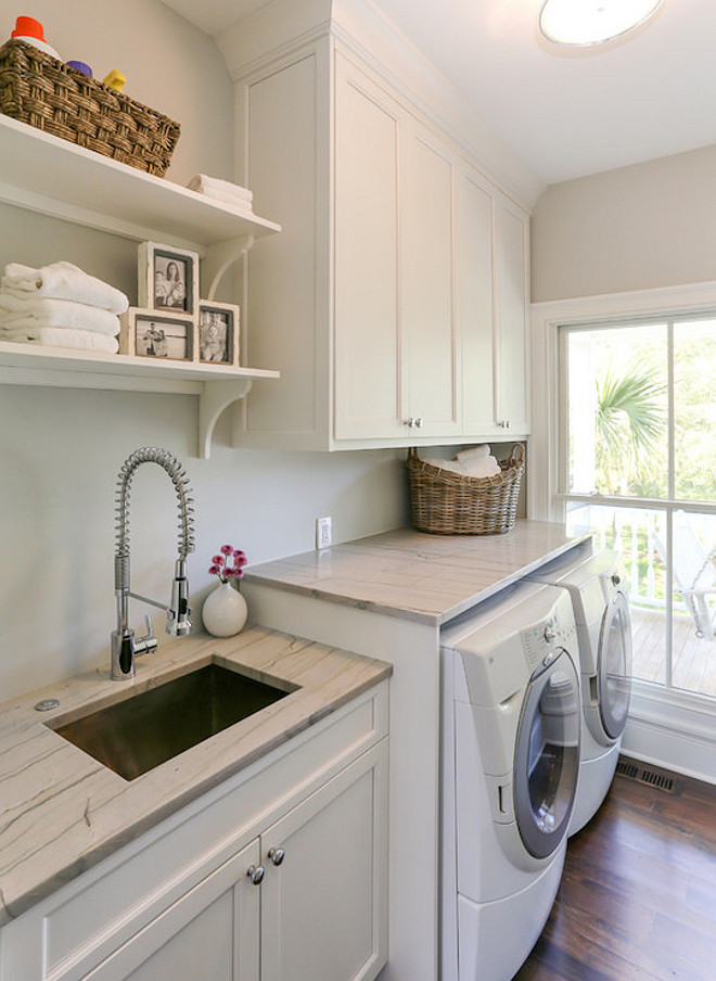 Laundry Room. Laundry room with white cabinets accented with nickel hardware and white quartzite countertops. The laundry room features a white front load washer and dryer below upper cabinets with an undermount sink paired with spray faucet to the right below open shelves. #LaundryRoom Charleston Home and Design