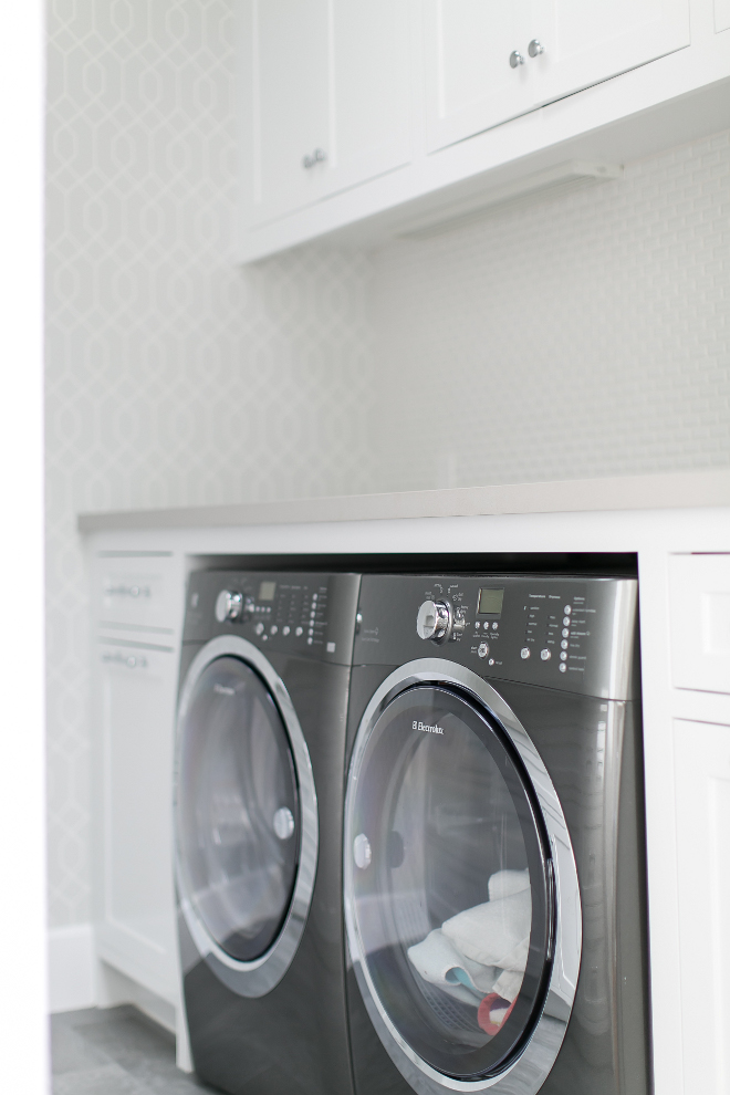 Laundry Room. This laundry room features a side by side, gray washer and dryer sat under light gray quartz countertops accenting white shaker cabinets fitted with polished nickel pulls. #LaundryRoom Churchill Design.