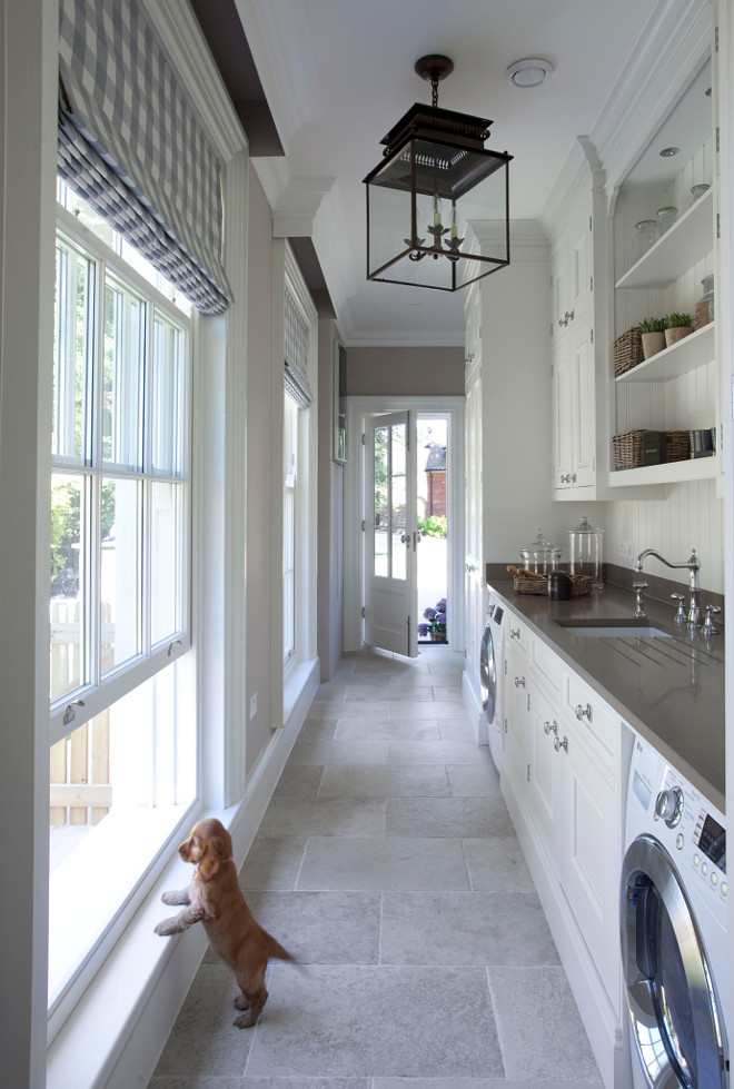 Mudroom and laundry room. This fabulous laundry room and mudroom features crisp white cabinets flanked by front-load washer and dryer topped with gray quartz countertop The windows are dressed in white and gray gingham roman shades. Countertop is Sinquastone Quartz in Bourbon. Faucets is Perrin & Rowe. Lighting is a Honore Hanging Lantern. Hayburn & Co. 