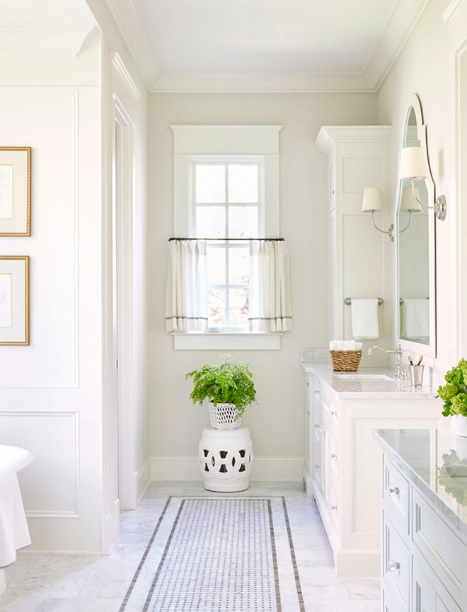 Ivory Bathroom. bathroom features separate washstands topped with polished marble fitted with square curved sinks and vintage hook and spout faucets placed under white arched mirrors illuminated by Vendome Single Sconces. A white marble tiles frame marble basketweave tiles accented with gray border tiles lead to a white rope stool topped with a fern plant placed under a window dressed in white and gray cafe curtains. #ivorywhite #bathroom Sarah Bartholomew Design