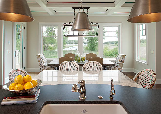 Kitchen nook. Kitchen island opens to kitchen nook. Countertop is Absolute Black Honed Granite. The dining room features a custom salvaged wood dining table and host chairs in a Kravet fabric. Side chairs are from Cisco. Dining room lighting is Darlana Linear Chandelier from Visual Comfort. #kitchennook #kitchenisland #kitchenlayout Vivid Interior Design. Hendel Homes