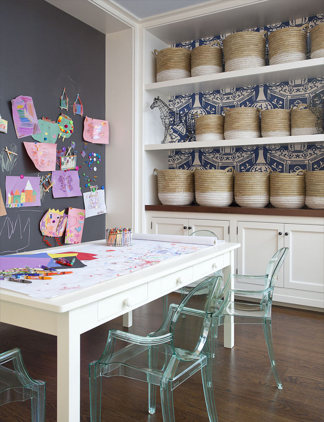 Playroom Chalk Wall. Kids playroom boasts a chalkboard accent wall placed in front of a white play table with drawers lined with Kartell Lou Lou Ghost Chairs in across from alcove clad with white and blue vase wallpaper, David Hicks The Vase Wallpaper, lined with white floating shelves filled with white dipped baskets over built in cabinets topped with wood countertop. #kidsplayroom #playroom #chalk #chalkwall Anik Pearson Architect