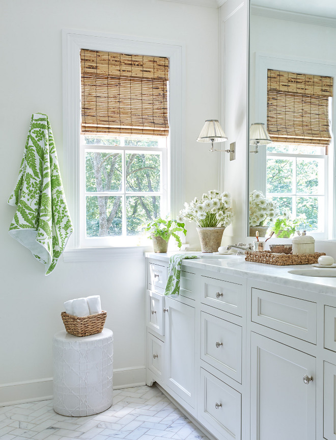 v White Bathroom with Green Accents and Marble Herringbone Floor. Beautifully designed white bathroom is clad in marble herringbone bathroom floor tiles accenting a white washstand fitted with polished nickel hardware and a marble countertop topped with a seagrass tray positioned beneath a white metal framed vanity mirror lit by a nickel sconce with a white pleated shade. A white lattice garden stool sits under a window dressed in a bamboo roman shade. White Bathroom with Green Accents and Marble Herringbone Floor # WhiteBathroom #GreenAccents #MarbleHerringboneFloor Sarah Bartholomew Design
