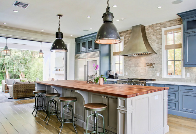 Blue Kitchen Cabinets with Gray Island. Blue & Grey Industrial Kitchen. This blue and grey industrial kitchen feature black industrial light pendants hung above a long light gray kitchen island with stained wood countertop and industrial counter stools. Blue cabinets are topped with a white marble countertop flaking a stainless steel oven range positioned beneath a steel hood mounted on travertine backsplash tiles. Kitchen feature blue cabinets and and grey island. #Bluecabinets #greyisland #IndustrialKitchen Matt Morris Development